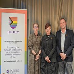 Three people standing next to a rainbow UQ Ally banner