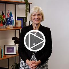 Professor Deborah Terry, UQ Vice-Chancellor, standing in front of a bookshelf. A play button has been digitally superimposed into the centre of the image.