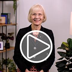 Vice-Chancellor Professor Deborah Terry in an office in front of a modern bookshelf, a pot plant and a lamp. A play button has been digitally added to the centre of the image.
