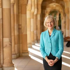 Professor Deborah Terry, UQ Vice-Chancellor, standing in a sandstone walkway and smiling