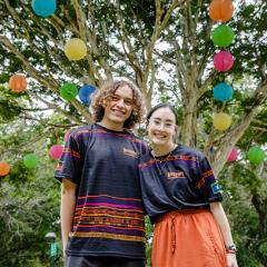 Two people with their arms around each other and smiling while wearing t-shirts with Indigenous artwork on them
