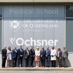 A group of people standing outside a building that has the UQ and Ochsner logos displayed