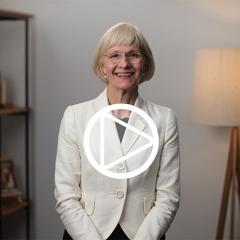 Professor Deborah Terry, UQ Vice-Chancellor, standing in front of a bookshelf. A play button has been digitally superimposed into the centre of the image.